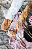 French bread on a linen cloth with a jar of jam and knifes and plates