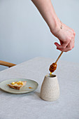 Hand mit Honiglöffel, daneben Honigbrot auf Teller