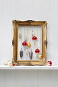 Vintage Christmas-tree baubles hung in gilt picture frame