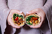 A woman holding a burrito with fried, diced potatoes, tomatoes, cream cheese, cheddar and spinach