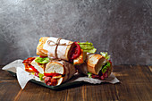 Fresh baguette sandwiches bahn-mi styled with bacon, roasted cheese, tomatoes and lettuce on wooden background