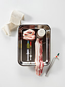 Pork belly with acupuncture needles, syringes, bandages, tweezers and tablets
