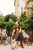 Dunkelhaarige Frau in braunem Kleid mit Hunden auf Bank sitzend