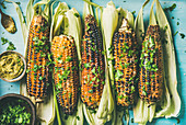 Grilled sweet corn with smoked sea salt, cilantro and pesto sauce over blue background