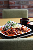 Schweinekotelett mit Sauce, Gemüsesalat und Reis auf Tisch (Asien)