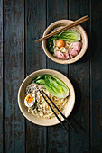 Asian dish with udon noodles with boiled egg, sesame, mushrooms, boc choy, sous vide pork meat served in ceramic bowls