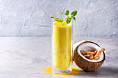 Cup of ayurvedic drink golden coconut milk turmeric iced latte with curcuma powder, crushed ice, mint