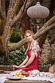 Junge Frau in rotem Kleid am Gartentisch