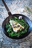 Hake on sauteed spinach in a frying pan