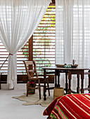 View across bed to wooden table in front of windows with louvre blinds