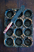An empty muffin tins with cake crumbs and a palette knife