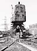 A blonde woman wearing a black jacket and white jeans on an industrial site (black-and-white shot)