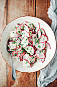 Radish salad with yogurt and poppy seed dressing in a white ceramic bowl on a wooden background from top view