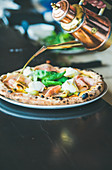 Freshly baked pizza with artichokes, smoked turkey ham, olives, cream cheese and basil on table in restaurant, selective focus