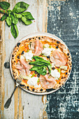 Freshly baked pizza with artichokes, smoked turkey ham, olives, cream cheese and green basil leaves on plate