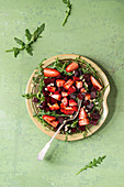 Beetroot and strawberry salad served with arugula and nuts on ceramic plate with fork over green texture background