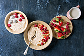 Sweet rice porridge pudding in ceramic plates with berries strawberry and raspberry, walnuts, mug of milk over blue texture background