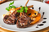 Roasted lamb ribs with grilled pumpkin and sause on white plate with red wine and seasonings