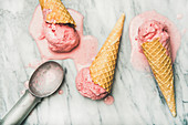 Yogurt strawberry ice cream in waffle cones over grey marble background