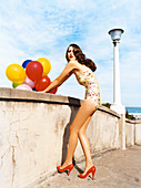 A brunette woman wearing a bathing suit and holding balloons