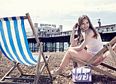 Junge Frau in hellem Top und Hose sitzt im Liegestuhl am Strand