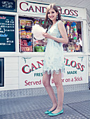 Young woman wearing pale blue dress and matching ballet flats holding candyfloss