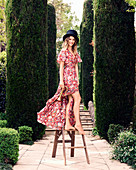 Junge Frau mit Zylinder in Sommerkleid auf einem Tritthocker im Park