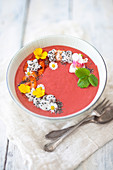 Erdbeer-Smoothie-Bowl mit Banane, Haferflocken, Drachenfrucht und Essblüten in einer Schale (vegan)