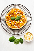 A pumpkin and feta cheese tart with basil leaves on a wire cooling rack