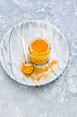 Turmeric in a jar with spoon on a light background