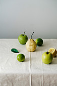 Äpfel, Birne, Limetten und Zitronenhälfte auf weisser Tischdecke