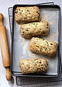 Pumpkin seed bread rolls on a baking tray with a rolling pin