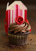 A chocolate cupcake with a cream topping and a marzipan rose