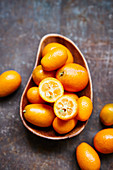 Kumquats, whole and halved, in a wooden bowl