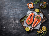 Two fresh raw salmon steaks on paper with salt, peppers, lemon, and rosemary