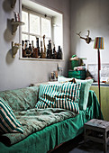Green blankets and cushions on sofa below window with ornaments on windowsill
