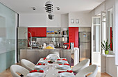 Set dining table in front of open-plan kitchen with red accents