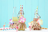 Bottles of lemonade decorated with paper strips and fabric flowers