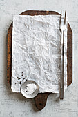 Pergamentpapier auf Holzschneidebrett mit Fleischgabel, Salz und Pfeffer