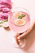 Frauenhand hält ein Glas rosafarbenen Cocktail mit Feigenscheiben