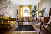 Mustard-yellow sofa, sideboard, table and chairs below window and potted palm in living room