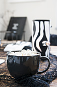 Hot drink topped with marshmallows in black cup in front of handmade tealight holder