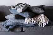 Stapel gefalteter Wolldecken und Kissen auf dem grauen Sofa