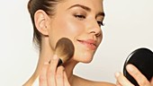 Woman applying face powder, studio shot