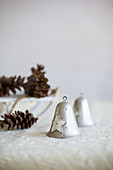 Two vintage-style bells and pine cones on white blanket