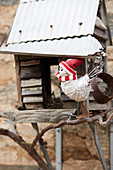 Winterlich gekleidete Vogelfigur vor Vogelhäuschen
