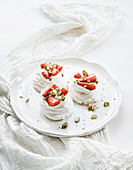 Small strawberry and pistachio pavlova meringue cakes with mascarpone cream