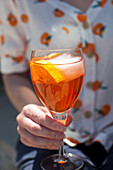 A woman holding a glass of Aperol Spritz with a citrus slice