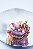 A blini topped with goat's cheese, red onions and roasted, flaked almonds