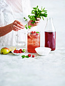 Einen Cranberry-Ingwer-Drink mit Beeren und grünen Blättchen dekorieren